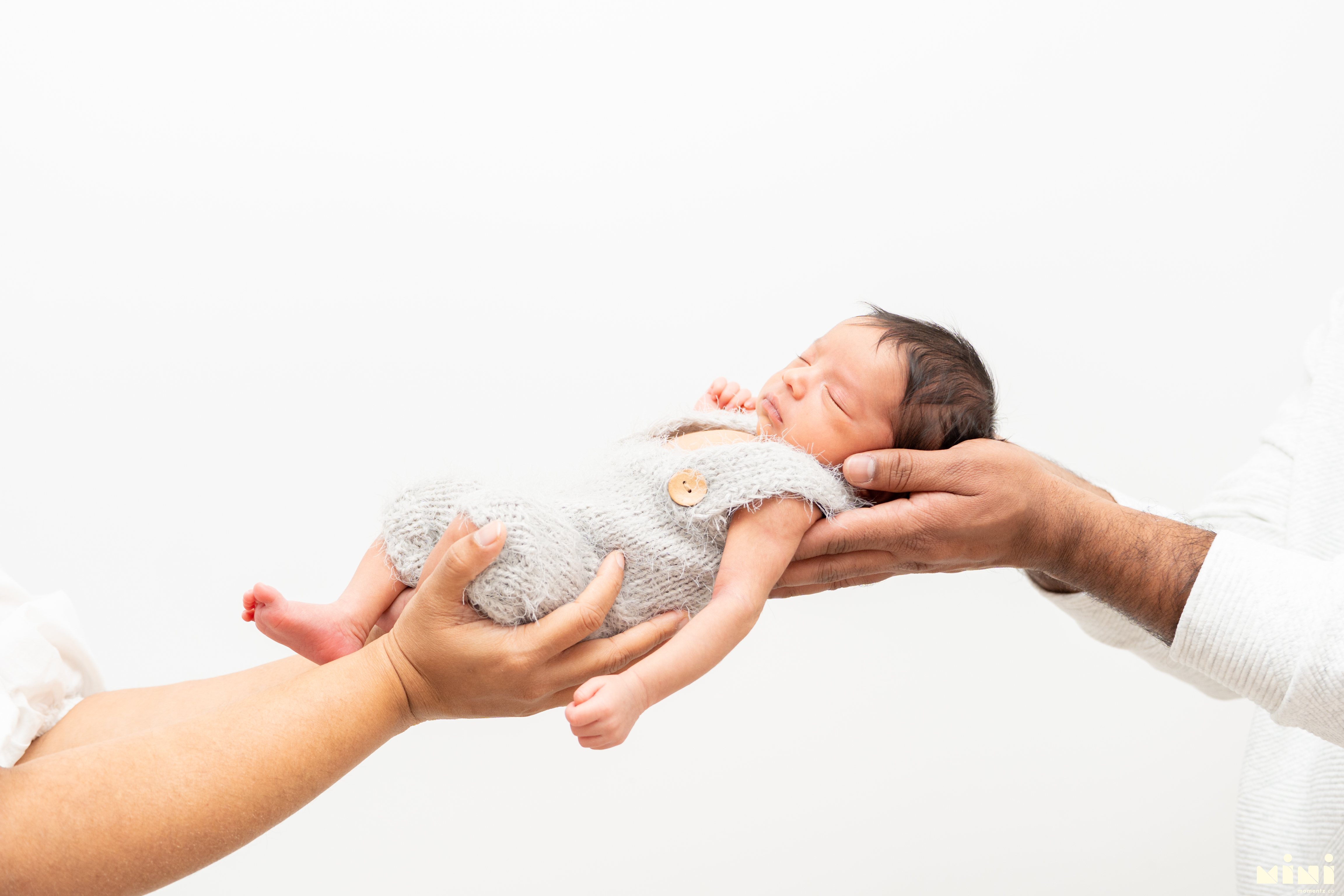 Chaithanya and Sowjanya gently passing their newborn daughter from hand to hand — one of the quietest, most tender images from the MiniMomentz Edinburgh newborn session