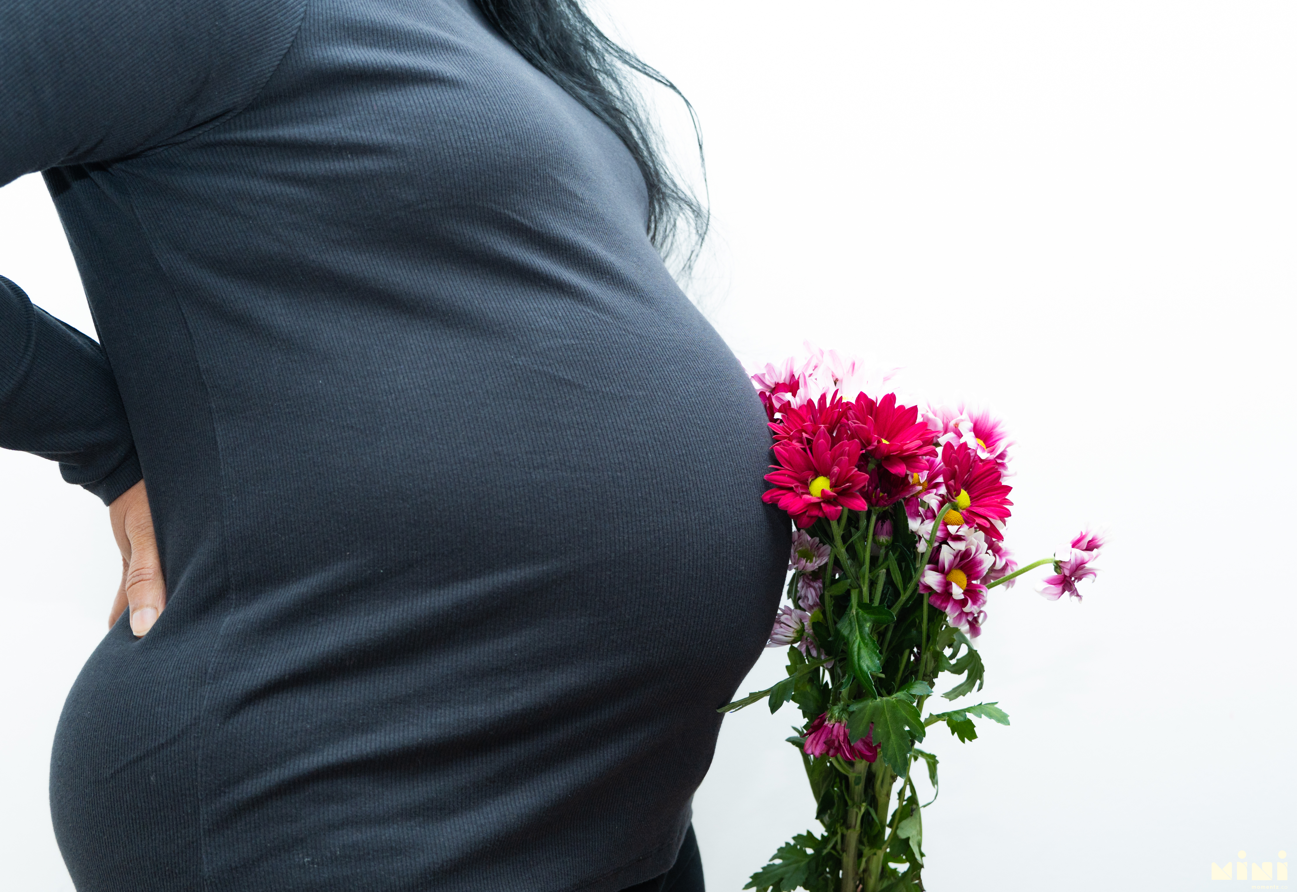 Close-up of Sowjanya's baby bump with a bouquet of pink and red flowers — maternity photography detail shot from the East Calder session with MiniMomentz