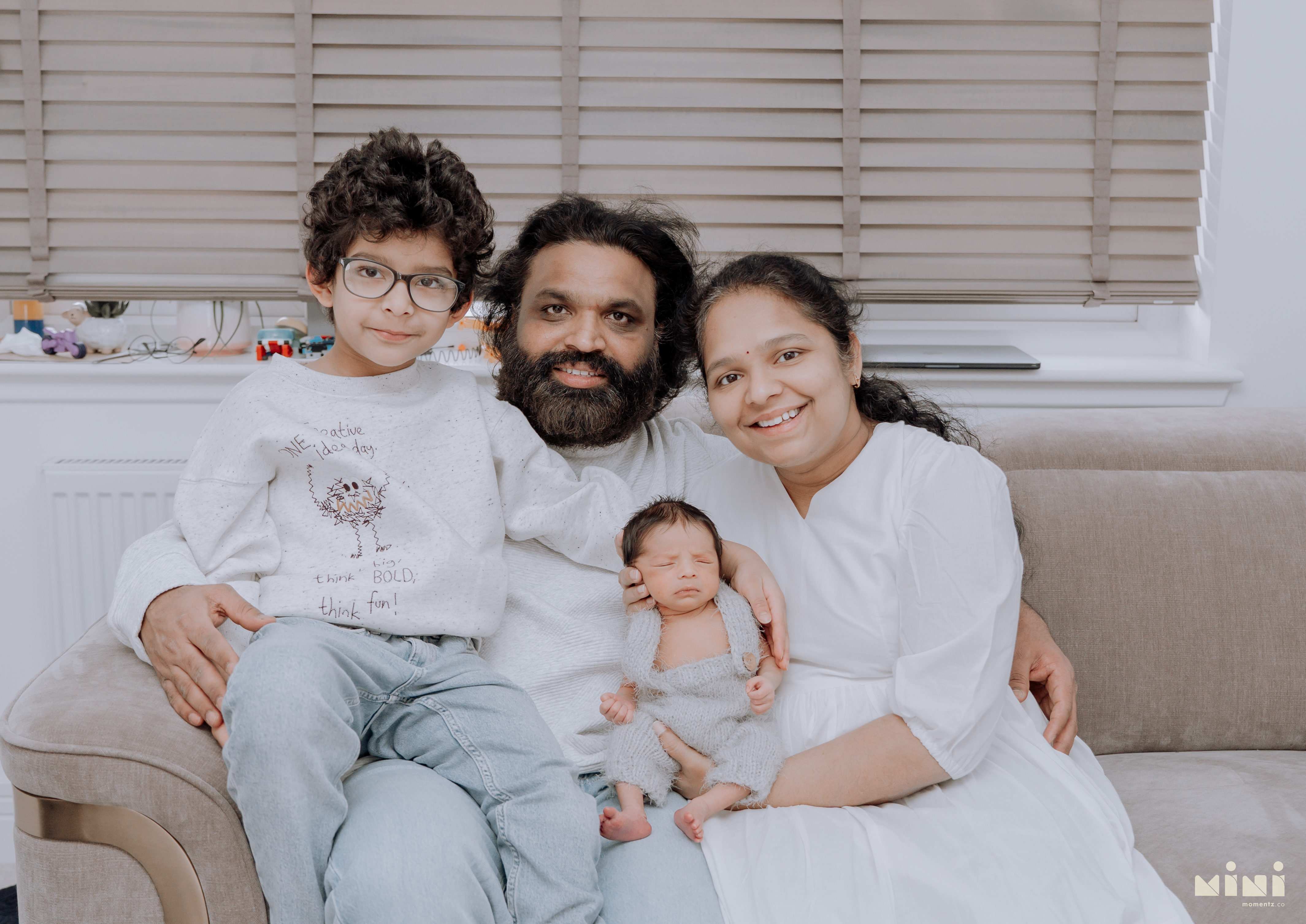 Chaithanya, Sowjanya, Kiwi and their newborn daughter together on the sofa — full family portrait from the Edinburgh home newborn session with MiniMomentz