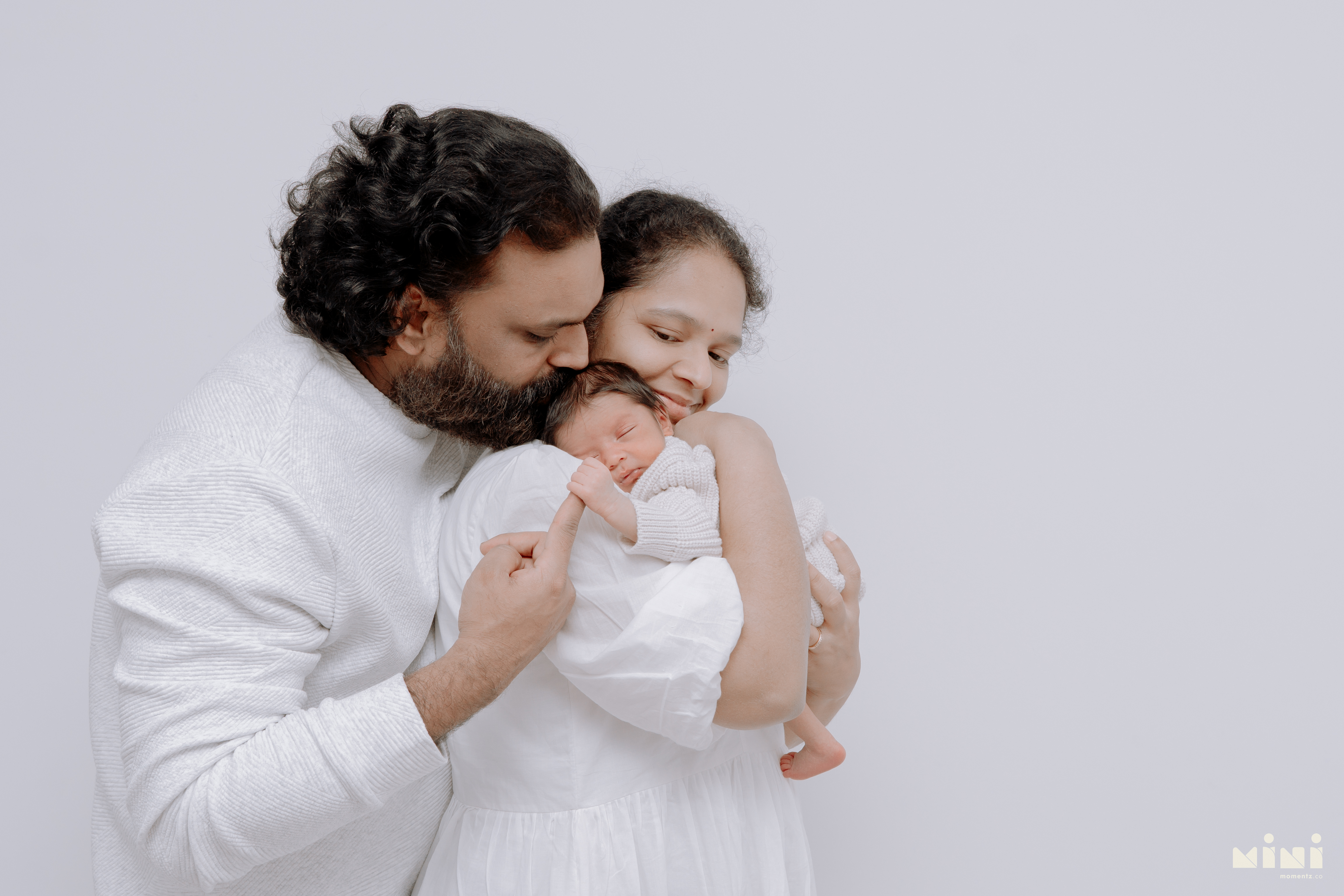 Chaithanya and Sowjanya gently holding their newborn daughter together during their Edinburgh newborn photography session with MiniMomentz