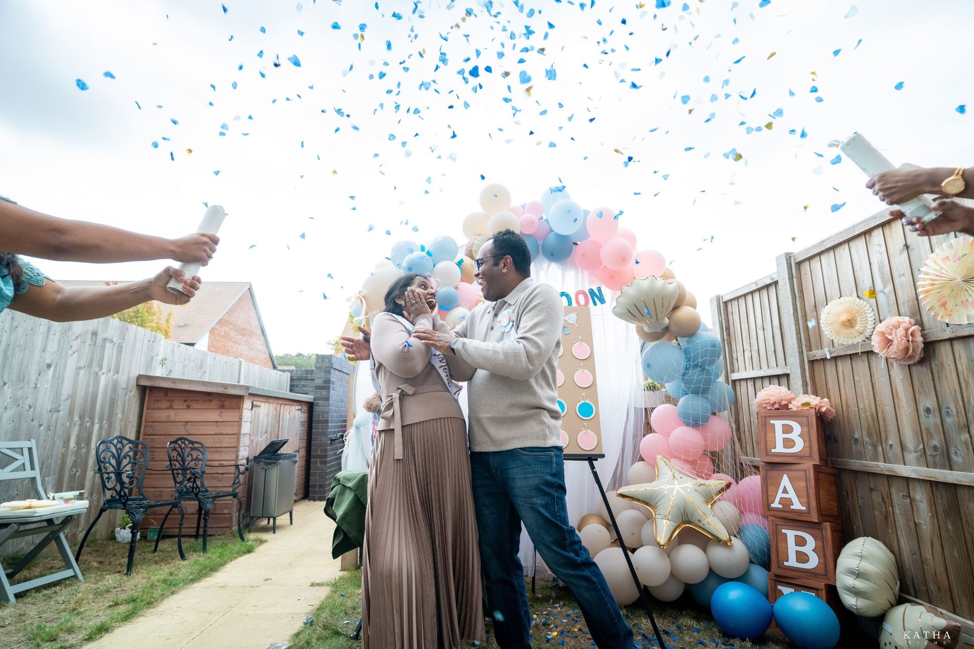 Sravanthi and Akhil celebrating beneath blue confetti at their gender reveal in Kent
